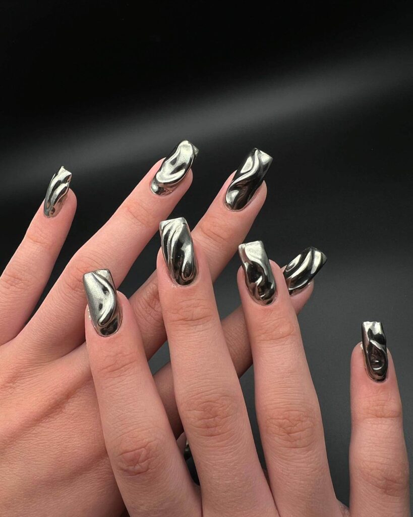 Close-up of hands showcasing various metallic nails designs, including black nails with silver flakes, dark gold nail polish, and metallic red acrylic nails.
